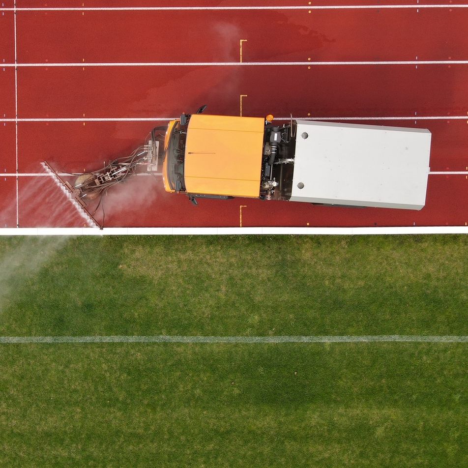 Eine Tartanbahn, die neben Rasen liegt und darauf fährt eine Reinigungsmaschine