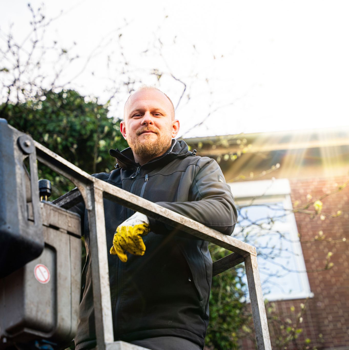 Lächelnder Mitarbeiter steht auf einer Hebebühne