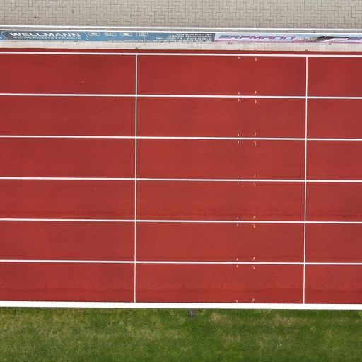 Nahaufnahme einer gereinigten Tartanbahn in rot direkt neben grünem Rasen