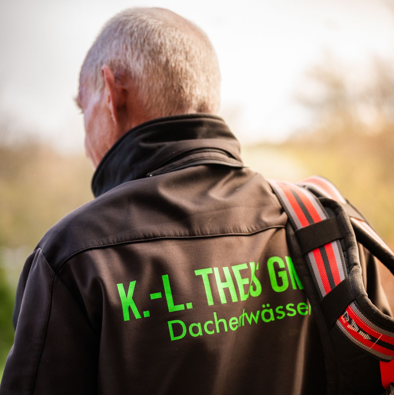 Mitarbneiter von hinten fotografiert trägt eine Jacke mit aufgedrucktem Theis-Logo