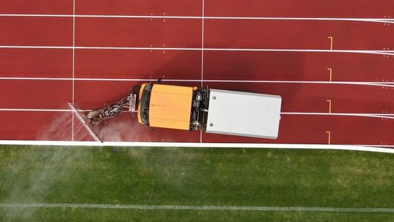 Eine Tartanbahn, die neben Rasen liegt und darauf fährt eine Reinigungsmaschine