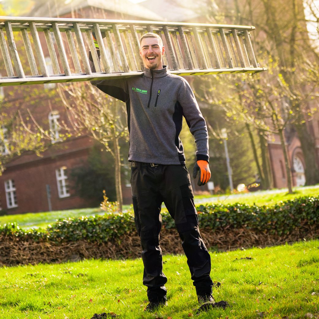 Mitarbeiter steht auf dem Rasen und trägt eine Leiter