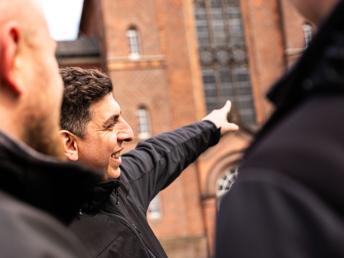 drei Mitarbeiter stehen im Kreis und zeigen auf die Fassade  einer Kirche