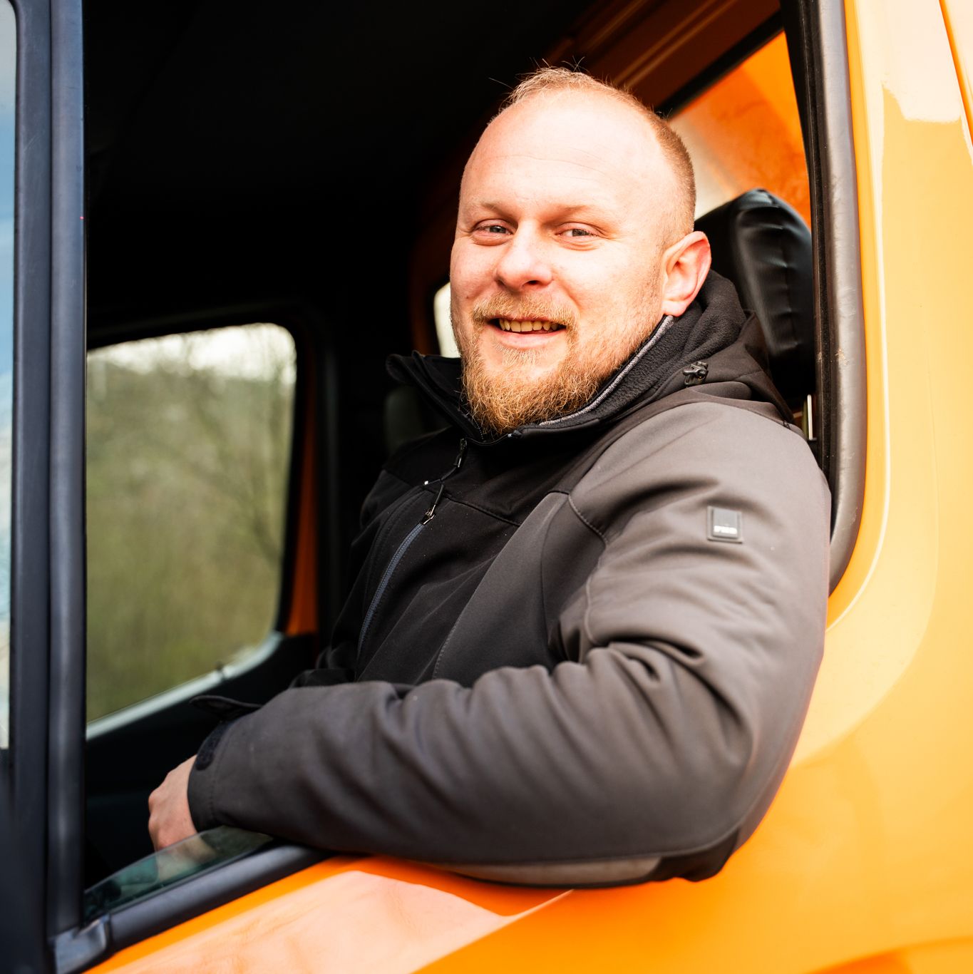Ein lächelnder Mitarbeiter sitzt auf der fahrerseite eines Fahrzeugs von Theis Spezialreinigung und lehnt cool seinen Arm aus dem offenen Fenster