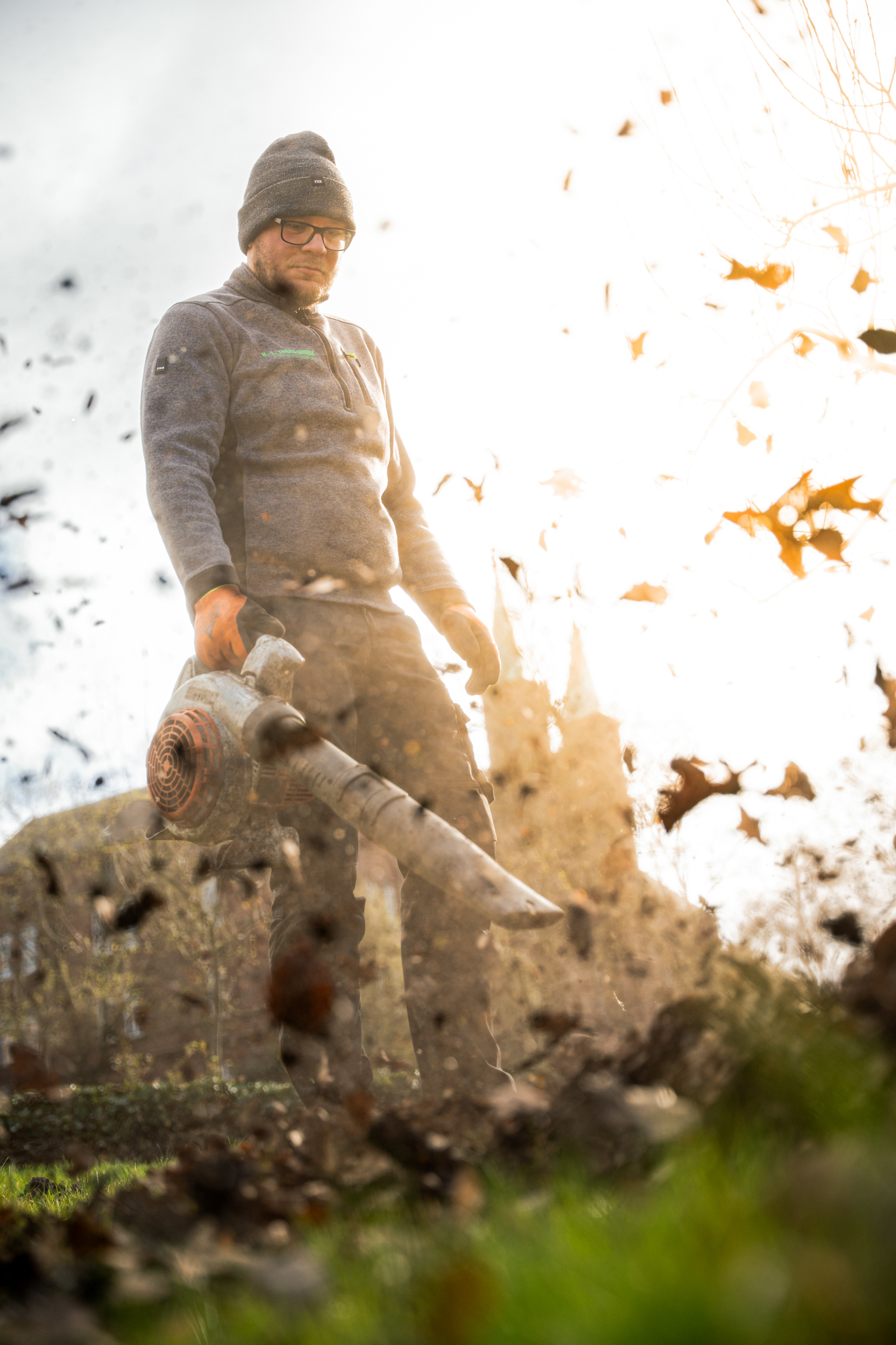 Mitarbeiter mit Laubgebläse und man sieht das Laub fliegen