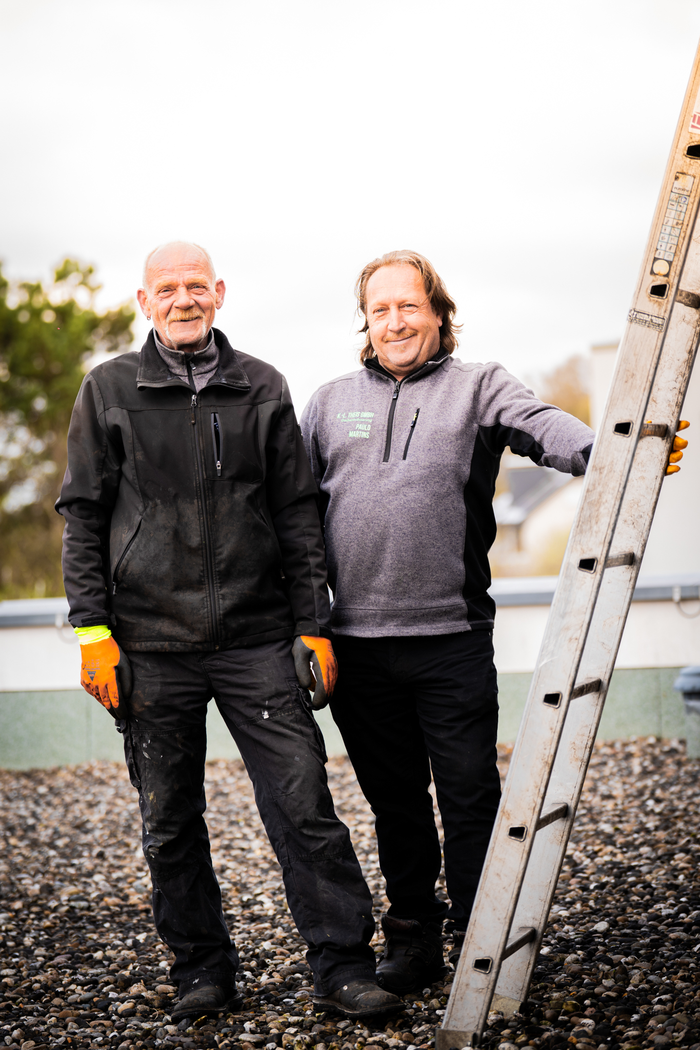 Zwei Kollegen nstehen nebeneinander und man sieht eine angelehnte Leiter